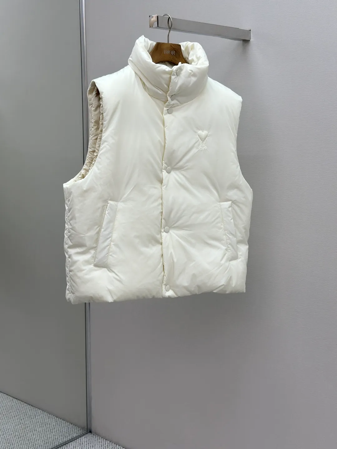 P810 AMIPARIS love padded embroidered down vest Fabric selection: Taffeta fabric woven from 100% polyester fiber. It adopts warp and weft plain weave and is woven very tightly, making the surface of the fabric extremely smooth and flat, with a "skinny" and stiffness that is not easy to collapse. When rubbed or moved around, it will make a unique, crisp "rustling" sound. At the same time, it has a delicate plain texture and a soft, elegant silky luster. This kind of luster is not as dazzling as satin, but more restrained and advanced.  Lining selection: Use 100% nylon to create the lining. The high-density and tight weaving process prevents tiny lint from getting out of the gaps in the fabric. The smooth surface improves the putting on and taking off experience, and the excellent wear and tear resistance ensures damage caused by frequent use, while the light and soft texture does not affect the overall weight.  Technology: The fabric and padding material are tightly fixed on the frame of the embroidery machine. The embroidery machine uses sparse stitches along the padding layer to outline the filling area of the pattern, and then runs the overlay layer's padding, using dense stitches to perfectly cover the foam padding layer, thus forming a slightly raised love embroidery, which feels soft and full, enhancing recognition while maintaining a low profile. High-quality filling: It uses 90 white duck down with a weight of 160g to ensure excellent thermal insulation performance. After strict screening and processing, the velvet is not easy to get drilled, ensuring durability.  Accessories: One-to-one customized three-standard, one-to-one customized hem elastic buckle, one-to-one customized snap button SIZE: XS S M L